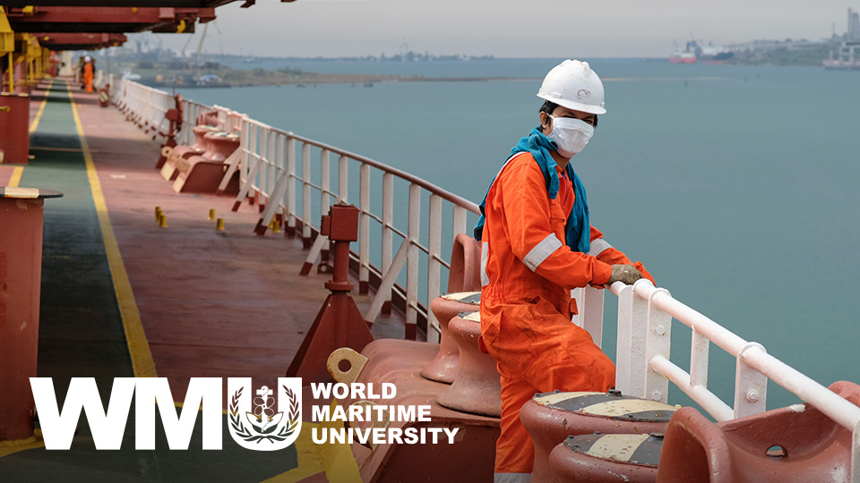 Crewman on cargo ship standing by the railing wearing a mask with World Maritime University logo superimposed in lower left corner.