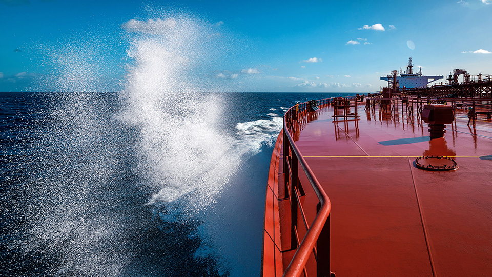 Sea water splashes on bow area of red super tanker heading towards the ocean horizon